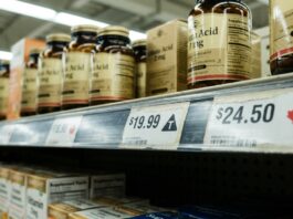 The T Is Back: What Loblaw’s Tariff Labels and Ottawa’s Counter-Tariff List Mean for Natural Health Grocery shelf label showing a triangle T tariff symbol beside a maple leaf Canadian product tag, supplement bottles above