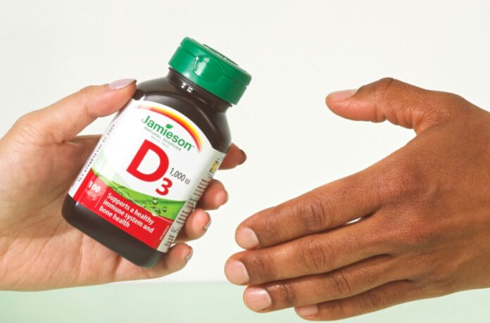 jamieson-wellness-kirin-shareholder-vote-hero Jamieson Wellness Kirin shareholder vote: a Jamieson vitamin D3 bottle handed from one person to another, illustrating the sale of the company to Kirin Holdings